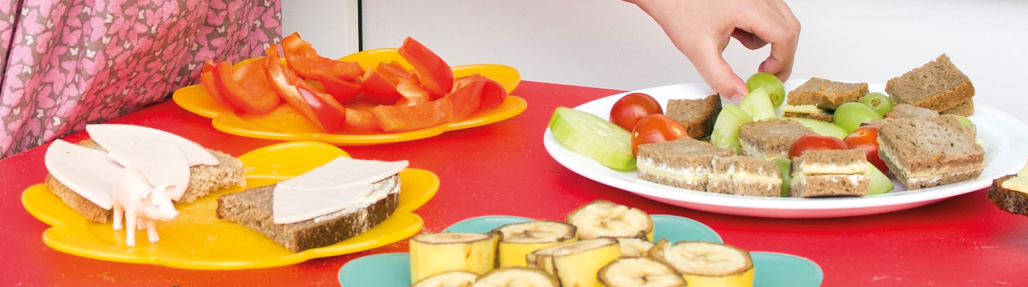 Ein kleines Mädchen steht vor einem Tisch mit gesundem Fingerfood. Sie nimmt sich eine Weintraube.